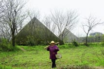 中国内陸部　巨大ピラミッドの前を鍬を担いだ女性が悠々闊歩