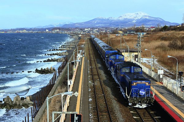 北海道・室蘭本線の北舟岡駅を通過する『北斗星』。全国有数の絶景の海に接した無人駅で、背後には雪化粧した有珠山を望む