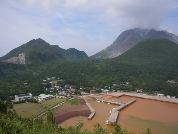 岬から硫黄島の港と集落を望む。火山活動の影響で海水が赤い