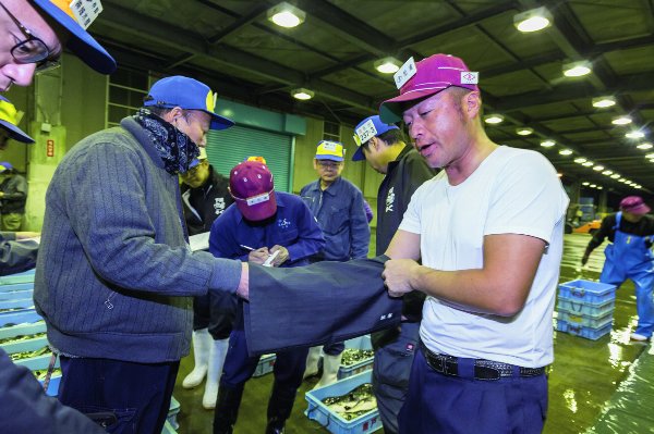 筒状の黒い袋に手を入れる「袋競り」の様子