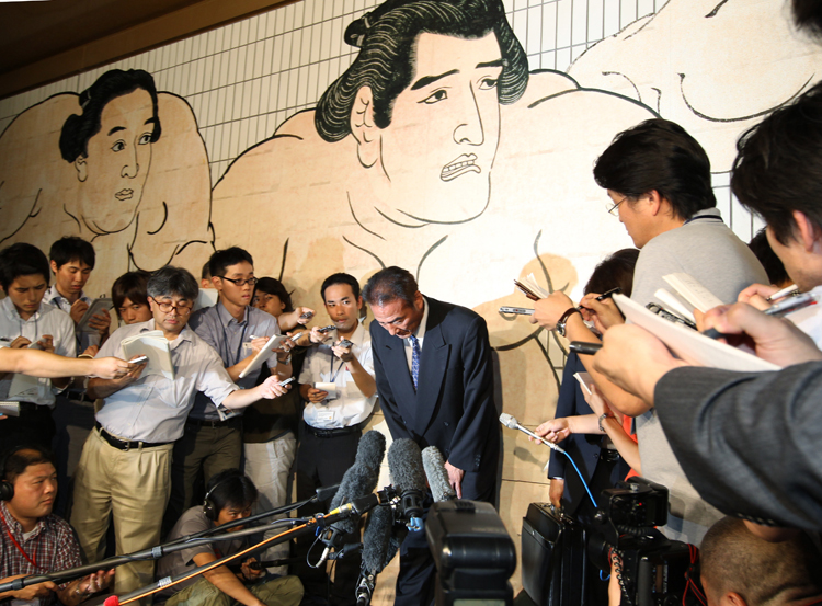 暴力団との関わりについての会見で、記者に囲まれ、頭を下げる松ケ根親方。（2010年7月、時事通信フォト）