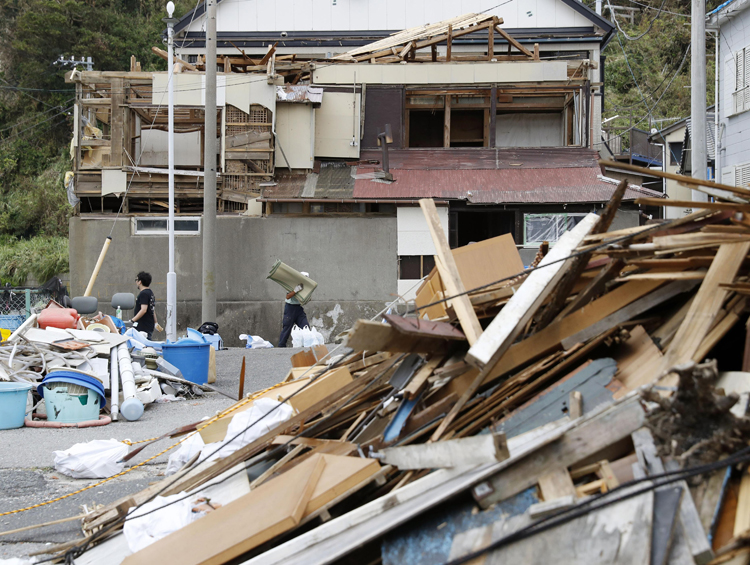 台風15号の影響で屋根や壁が壊れた家屋と積み上げられたがれき（千葉県鋸南町　写真／共同通信社）