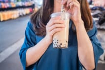A young woman is drinking a plastic cup of bubble milk tea with a straw at a night market in Taiwan, Taiwan delicacy, close up.