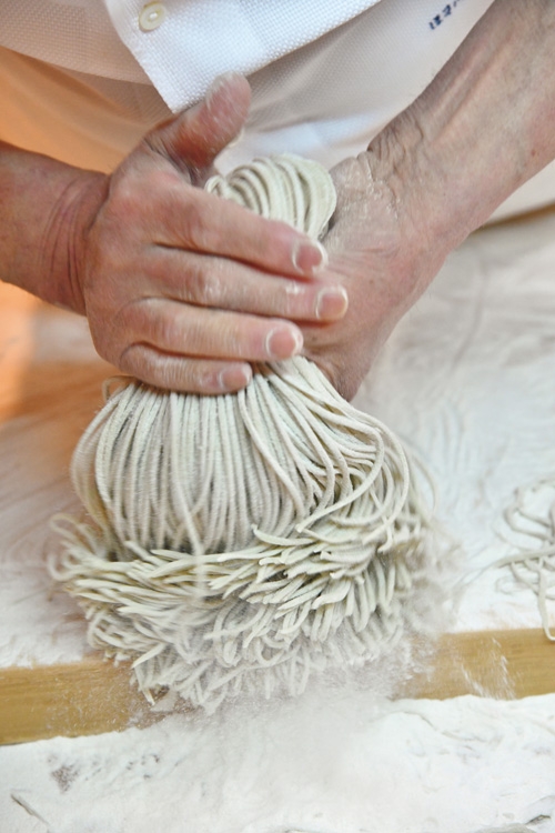 幅が均等になるよう切った蕎麦を包丁ですくい上げ、打ち粉を軽くはたく