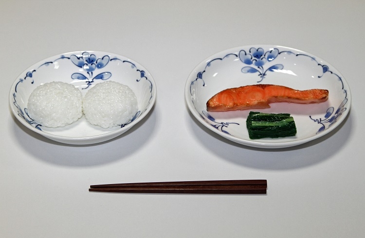 学校給食は長らく子供たちの栄養を支えてきた。明治22年の給食献立。おにぎり、塩鮭、菜の漬物。学校給食歴史館の展示サンプル(時事通信フォト)