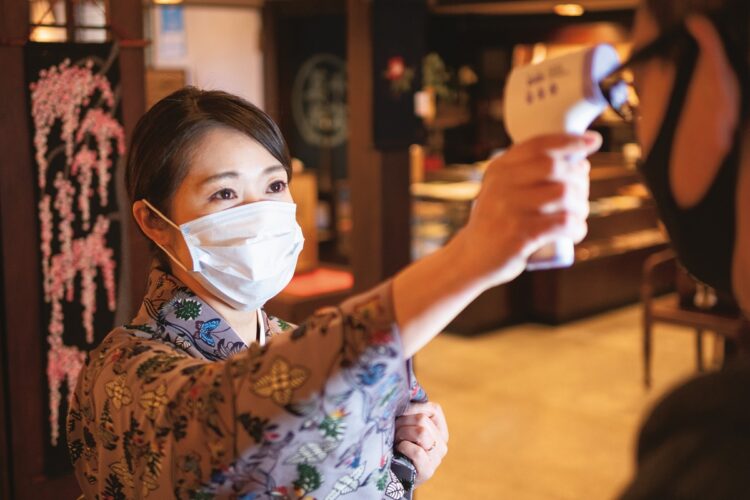 新型コロナウイルス対策で、到着した宿泊客の体温の測定を行なう二瓶さん。館内には各所に消毒液が置かれている