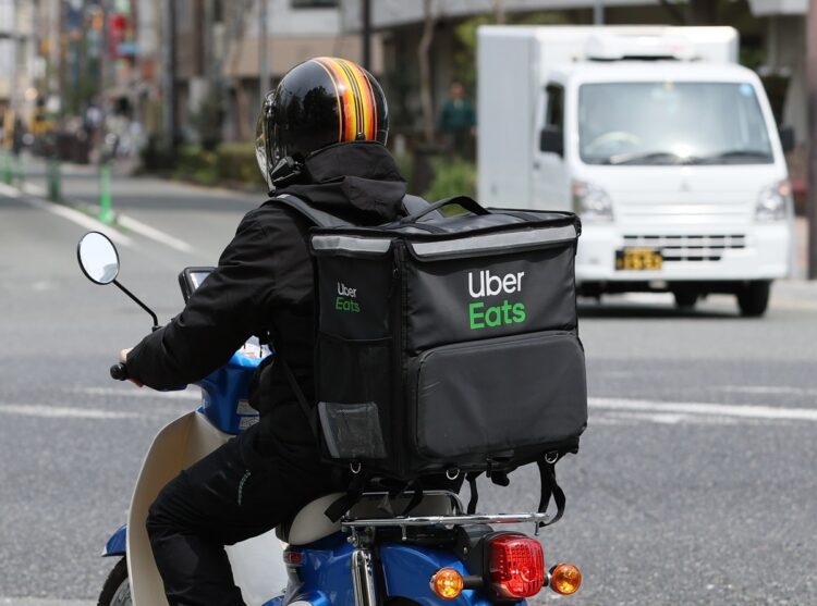 街中を走る「ウーバーイーツ」の配達員。ほとんどの配達員が自転車もしくは原付バイクで配達している（イメージ、時事通信フォト）