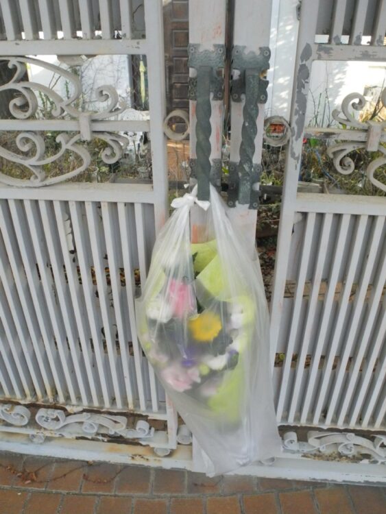 白亜の豪邸の門扉には花が手向けられていた