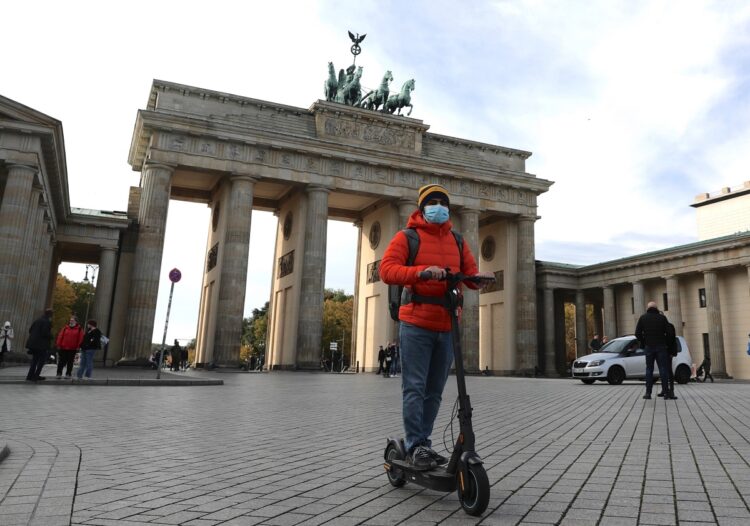 ドイツ・ベルリンのブランデンブルク門前を電動キックスケーターで移動する男性（EPA＝時事）