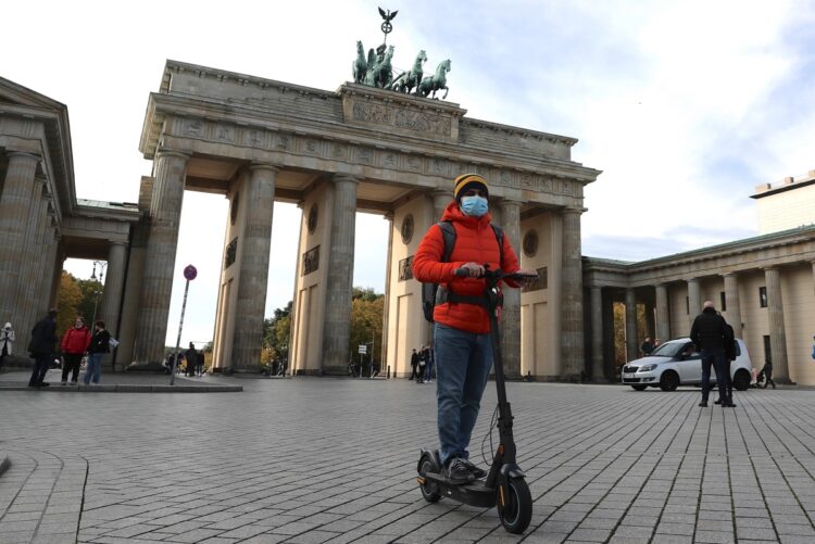 ドイツ・ベルリンのブランデンブルク門前を電動キックスケーターで移動する男性（EPA＝時事）