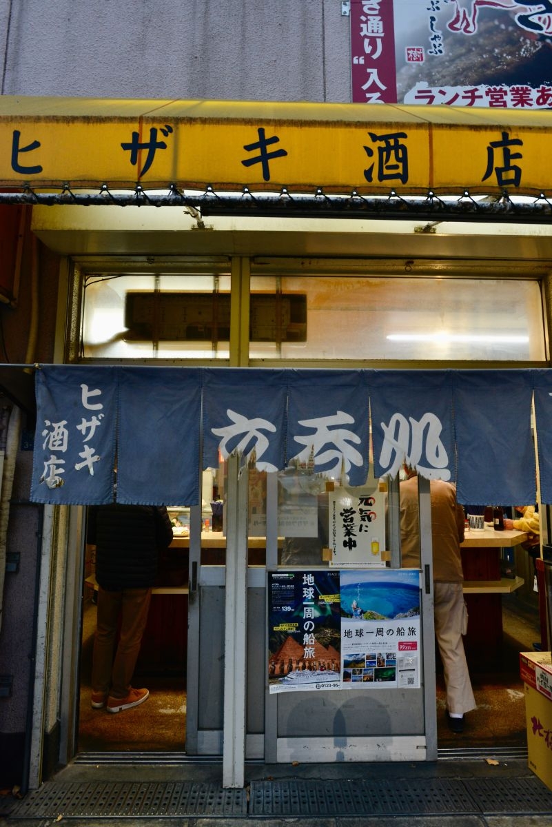 黄色の庇が印象的な店構えのヒザキ酒店