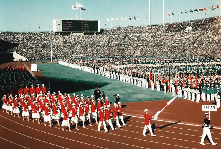 1964年、東京五輪。94か国が参加した前回東京大会の開会式。前日までの雨があがり抜けるような青空のもと、日の丸カラーの355人が入場行進した（写真／共同通信社）