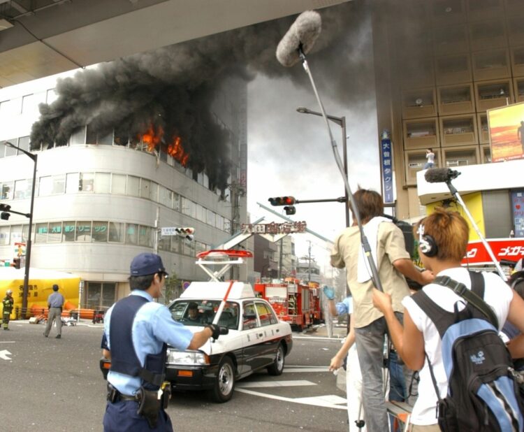 2003年、黒煙を上げ炎上する男が立てこもった名古屋市内のビルと騒然とする報道陣と警官ら（時事通信フォト）