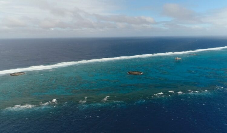 東西に4.5km、南北に1.7kmの環礁のなかに浮かぶ沖ノ鳥島と観測所、灯台（写真内右）。島に上陸するためには小型のボートに乗り換える必要がある