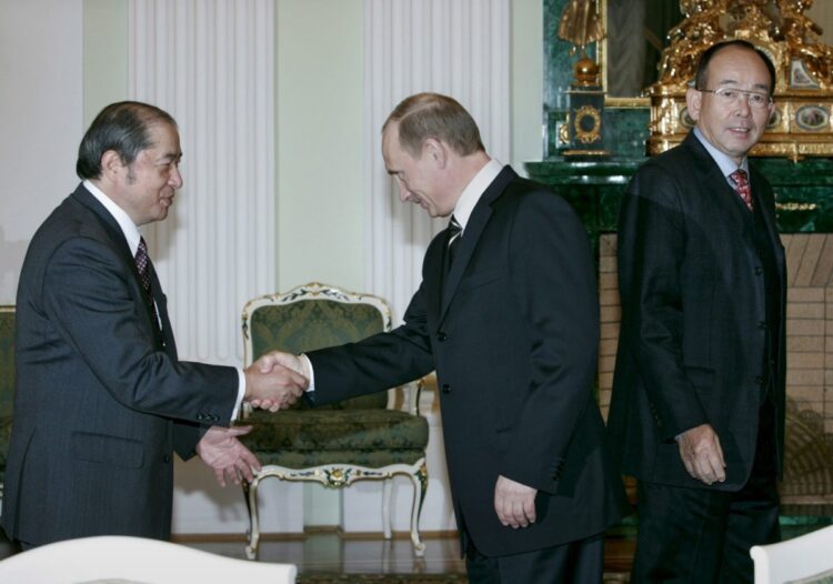 2006年12月、「サハリン2」の権益譲渡が行われたモスクワで、プーチン大統領（中央）と握手する当時の小島順彦三菱商事社長（左）と槍田松瑩三井物産社長。この結果、ロイヤル・ダッチ・シェル、三井物産、三菱商事の出資比率がそれぞれ半分に低下、ロシアの国営天然ガス独占企業ガスプロムが経営権を握ることになった（EPA＝時事）