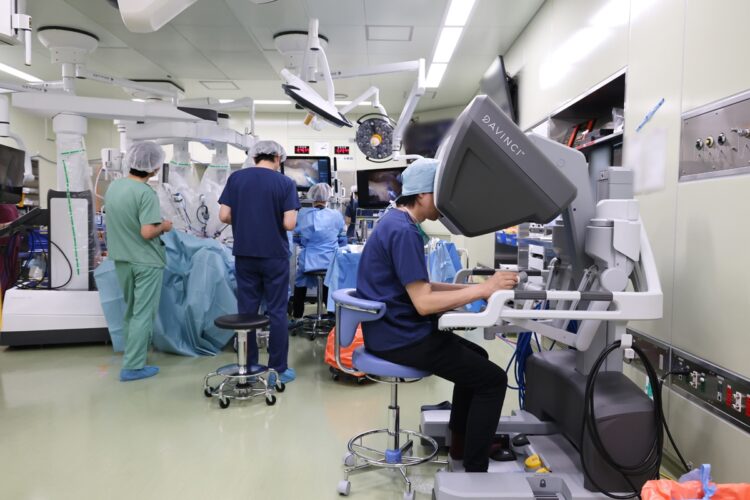 手前のサージョンコンソール（操縦席）で両手両足を巧みに使い、手術支援ロボット「ダ・ヴィンチ」を操作。見学している他病院の医師たちにも技術やアドバイスを惜しみなく伝える。今年４月から結腸がんに対するロボット支援下手術が保険適用になったことにより、新たに同手術を始める病院、医師が増えているという