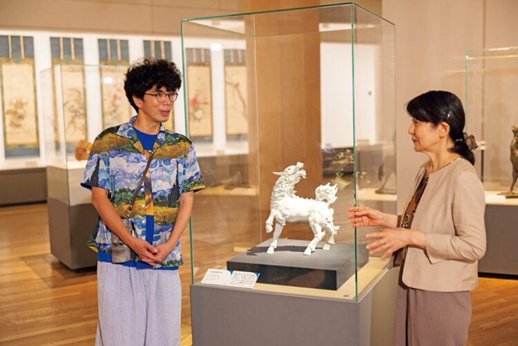 『白磁麒麟置物』十二代酒井田柿右衛門／昭和3年（1928） 宮内庁三の丸尚蔵館蔵（通期展示）の前で。黒川館長の明快な解説に興味津々の片桐さん