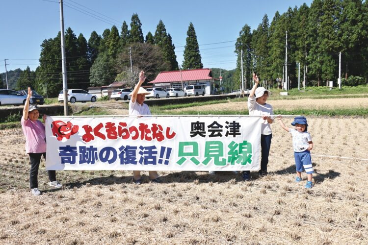 歓迎の横断幕を持って列車に笑顔で手を振る住民たち。10月1日は会津若松駅発の一番列車が非常ブレーキのトラブルで立ち往生し、一時、全線で運転見合わせとなったが、線路沿いでは多くの住民が運行再開を何時間も待ち続けていた（撮影／太田真三）