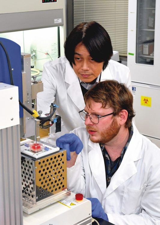 大阪大学・松崎典弥教授（奥）と、研究員のミュレール・カンタン氏。細胞を射出する3Dプリンターの動作について議論する
