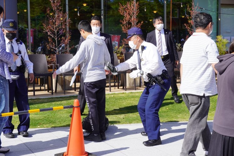 街頭演説会場で聴衆者に金属探知機を使ってボディーチェックをする警察官。2023年4月22日、和歌山市(時事通信フォト)
