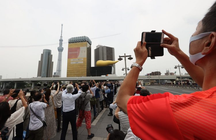 記念すべきものを見たら自然にスマホ撮影するようになった。東京パラリンピック開会式当日、東京上空を飛行する航空自衛隊の曲芸飛行チーム「ブルーインパルス」を眺める人たち。2021年8月（イメージ、時事通信フォト）