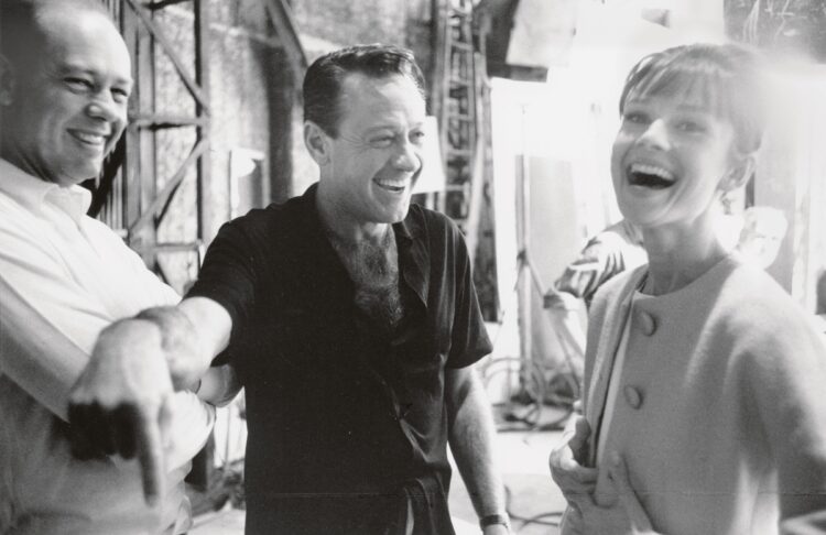 『パリで一緒に』（1964年）。脚本家とタイピスト、ガブリエルの恋を描くロマンチックコメディでは劇中劇で一人二役に挑戦。右から撮影中に談笑するオードリーと俳優ウィリアム・ホールデン、監督のリチャード・クワイン（写真＝Bob Willonghby／mptvimages／AFLO）