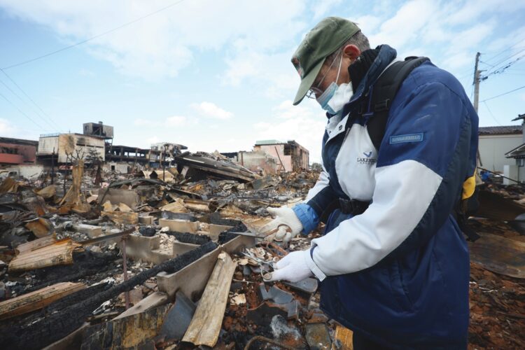 輪島市内の全焼した自宅から、妻の使っていた裁縫用のはさみを拾い上げて見入る男性（時事通信フォト）