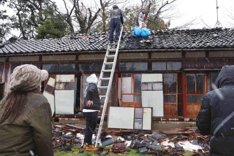 積雪の予報のあった日、地震の影響が生々しく残る建物にブルーシートをかけて備える被災者（時事通信フォト）