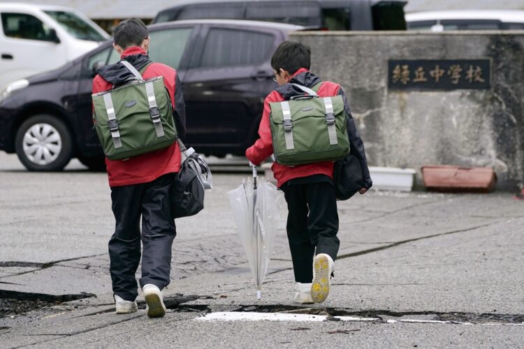 本来は１月９日に行われるはずだった珠洲市の小中学校始業式は、11日から少しずつ再開され始めた。写真は亀裂が入ったままの地面を歩き、登校する珠洲市立緑丘中学校の生徒たち（共同通信社）