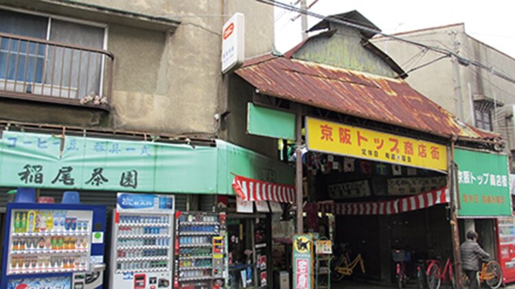手書きの「京阪トップ商店街」の黄色い看板とトタン屋根のひさしがレトロな味わいを加速させる