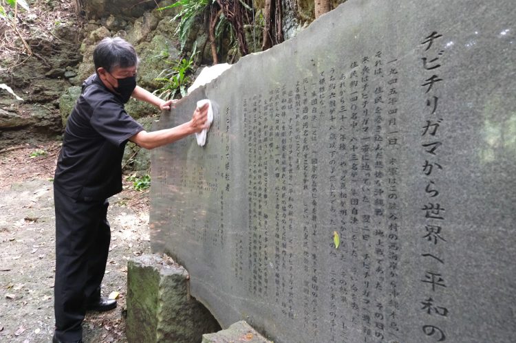 犠牲者の名前が刻まれた石碑を拭く遺族。沖縄県読谷村のチビチリガマ（時事通信フォト）