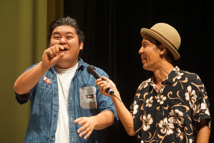 企画、脚本、演出、製作総指揮を一手に担うのは那覇市出身の芸人「まーちゃん」こと、小波津正光（右）