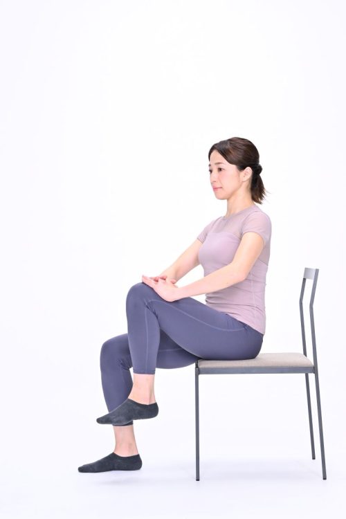 (1)椅子に浅く座り、左膝をへその高さまで引き上げる。へそが無理なら、股関節よりも高く上げる。両手のひらを組み、左膝に置く。
