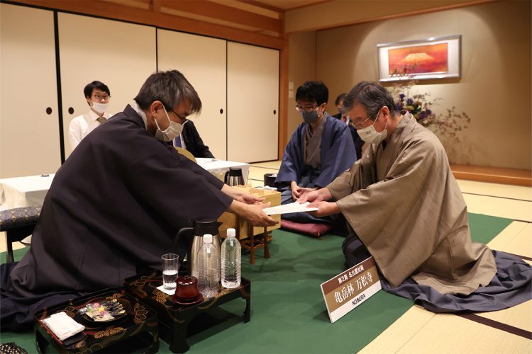 第33期竜王戦7番勝負第2局。「封じ手」の入った封筒を立会人の青野照市九段(右)に手渡す羽生善治九段。中央奥は豊島将之竜王(2020年10月22日撮影、時事通信フォト)